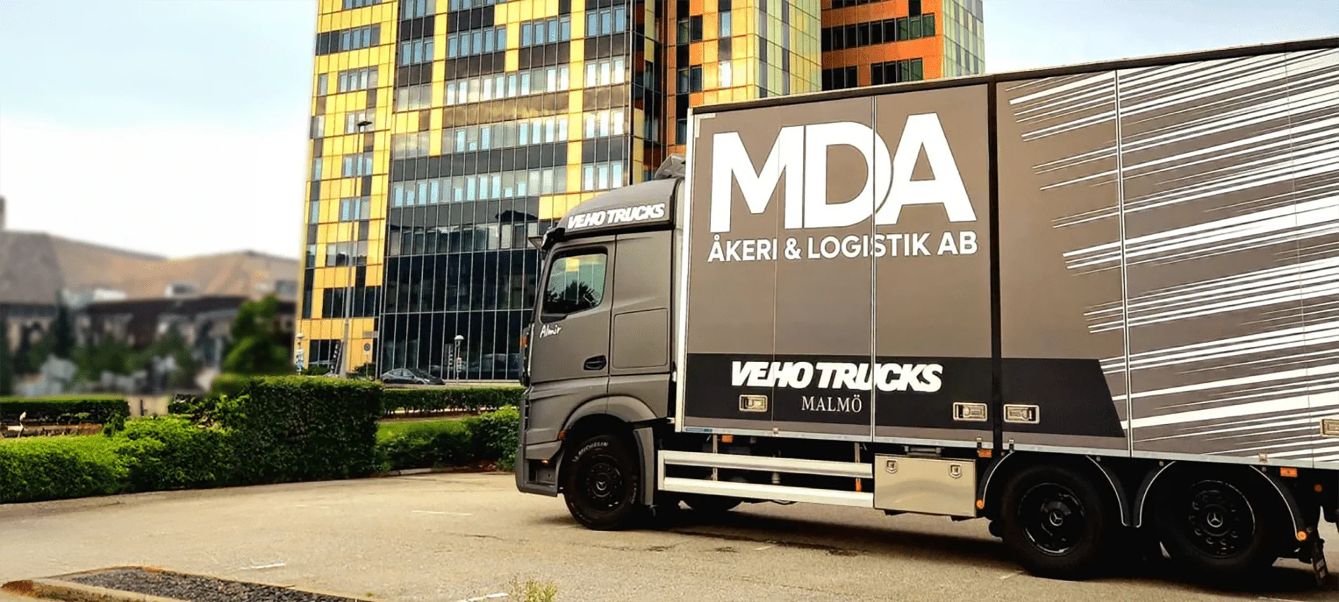 MDA:s lastbil med företagets logotyp på sidan, parkerad framför ett kontorshus